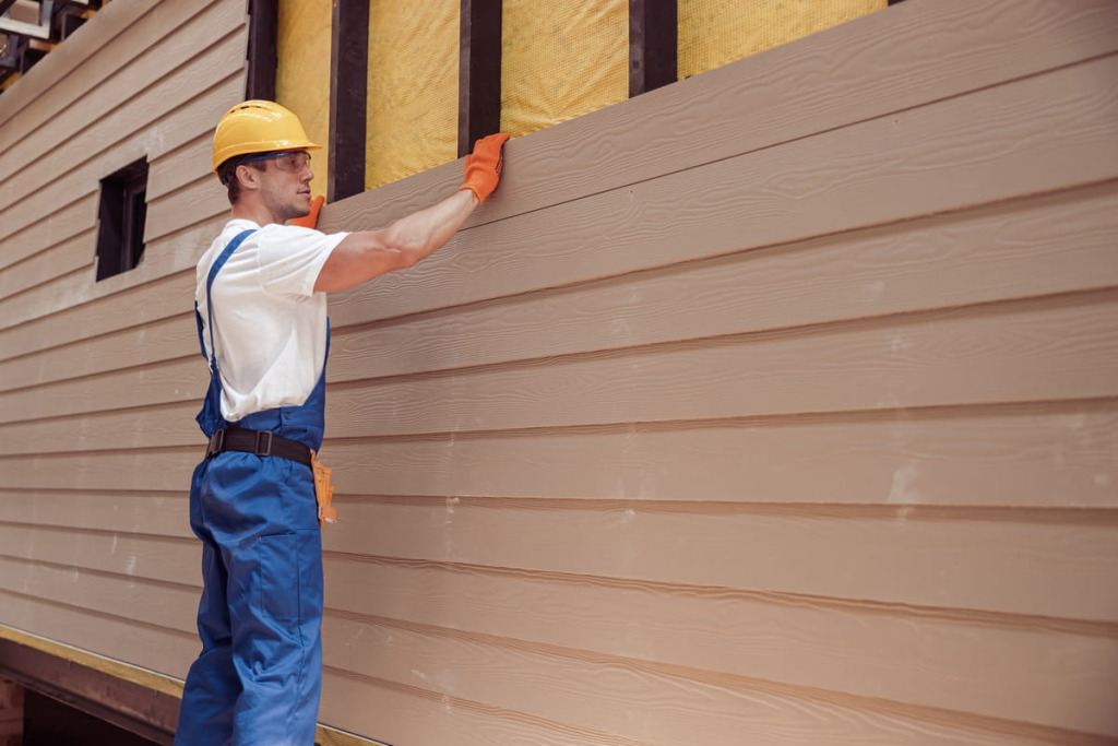 Siding contractor in safety gear installing horizontal lap siding over insulation on a home exterior